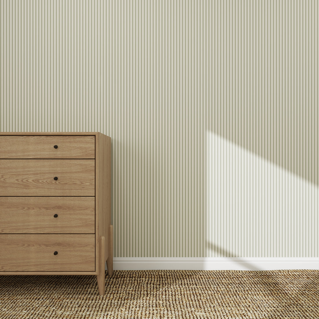 A wooden dresser with four drawers stands on a woven rug against Pico Stripe Wallpaper Green. Sunlight casts shadows on the wall and floor.