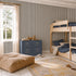 Children’s bedroom with wood bunk beds, a blue dresser with toys, a large tan pouf, and a yellow rug. The room features Pinstripe Wallpaper Charcoal for a playful touch and a window with sheer beige curtains letting in natural light—perfect for transitioning from nursery to kid’s space.