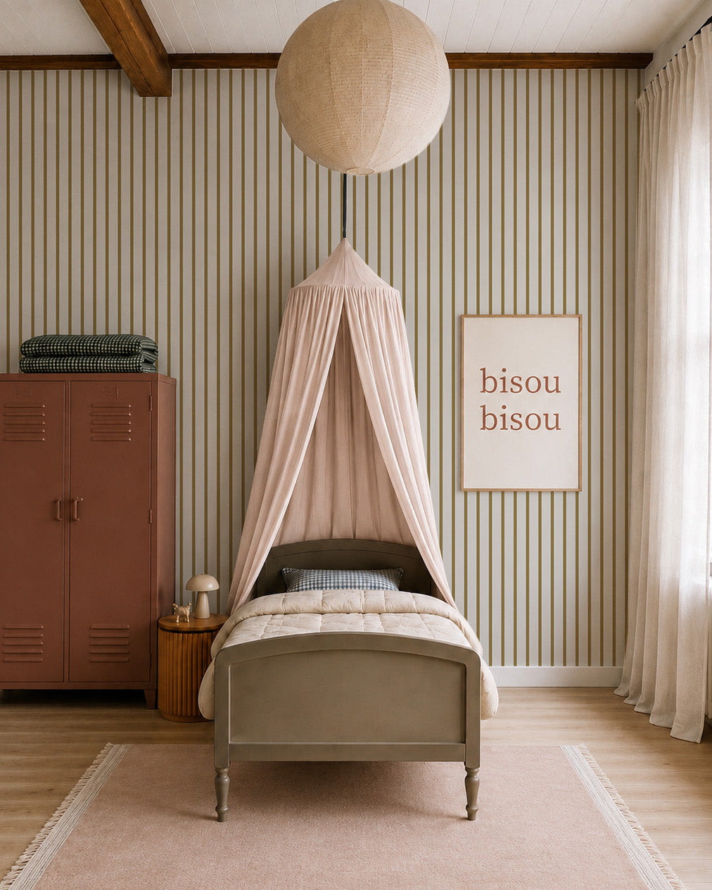 A cozy nursery features a single bed under a blush canopy, a large paper lantern, a pink wardrobe, framed "bisou bisou" art, and Pinstripe Wallpaper Moss adding warmth as sunlight filters through sheer curtains.