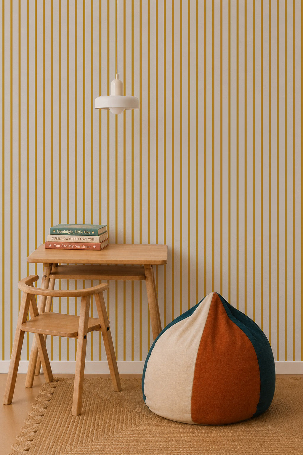 A minimalist room with a small wooden desk and chair, stacked books, a round beanbag in cream, orange, and green, and a hanging white lamp set against Pinstripe Wallpaper Mustard.