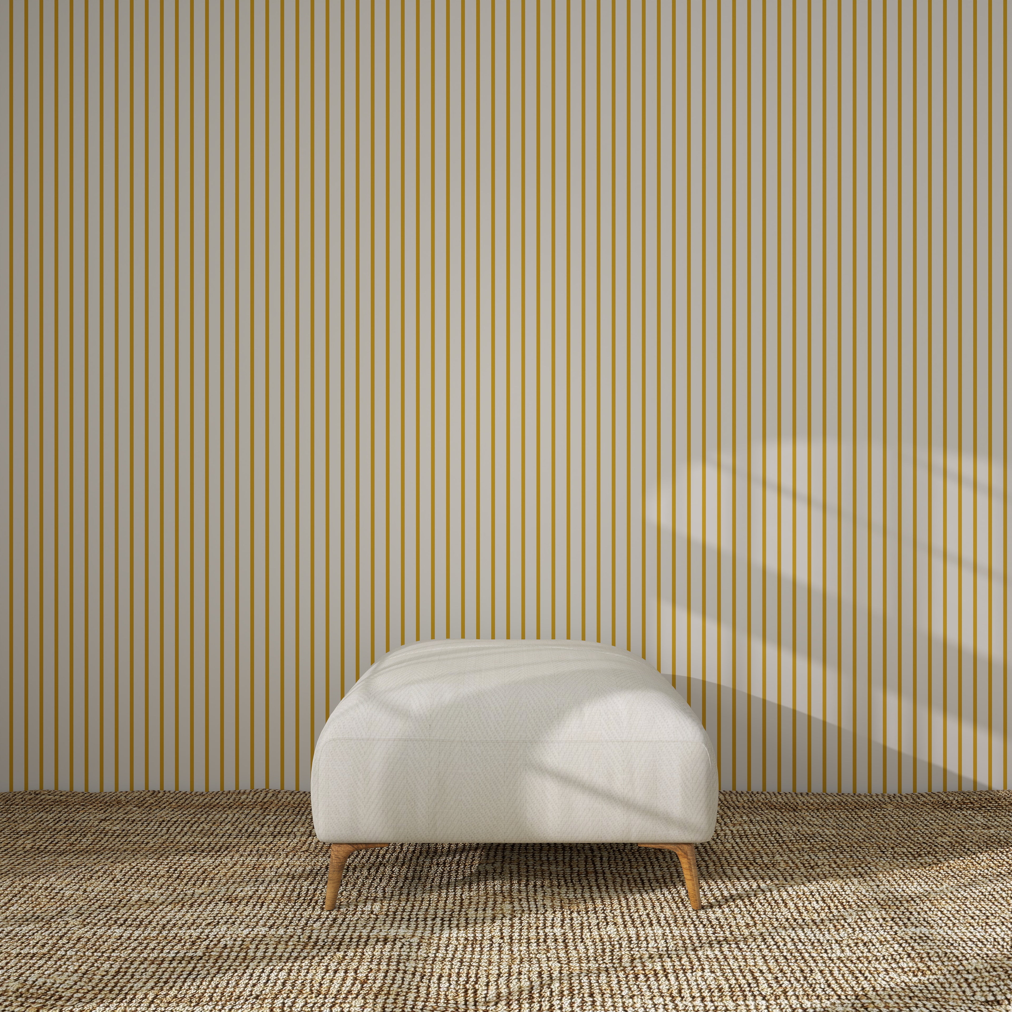 A minimalist room features a beige ottoman on a textured carpet, set against a wall with Pinstripe Wallpaper Mustard. Sunlight streaming through an unseen window casts soft shadows, adding warmth to the modern nursery decor.
