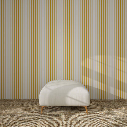 A minimalist room features a beige ottoman on a textured carpet, set against a wall with Pinstripe Wallpaper Mustard. Sunlight streaming through an unseen window casts soft shadows, adding warmth to the modern nursery decor.