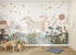 A children’s room featuring the Unicorn Meadow Wallpaper Mural, showing two unicorns among colorful flowers, leaves, and stars. The space includes a small wooden table with chairs, a blue floor cushion, a lamp, and built-in white cabinets.