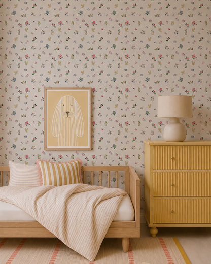 A cozy children’s bedroom features Powdered Petals Wallpaper, a wooden bed with striped bedding, a yellow dresser, matching lamp, and a framed bunny illustration in soft neutral and pastel tones.