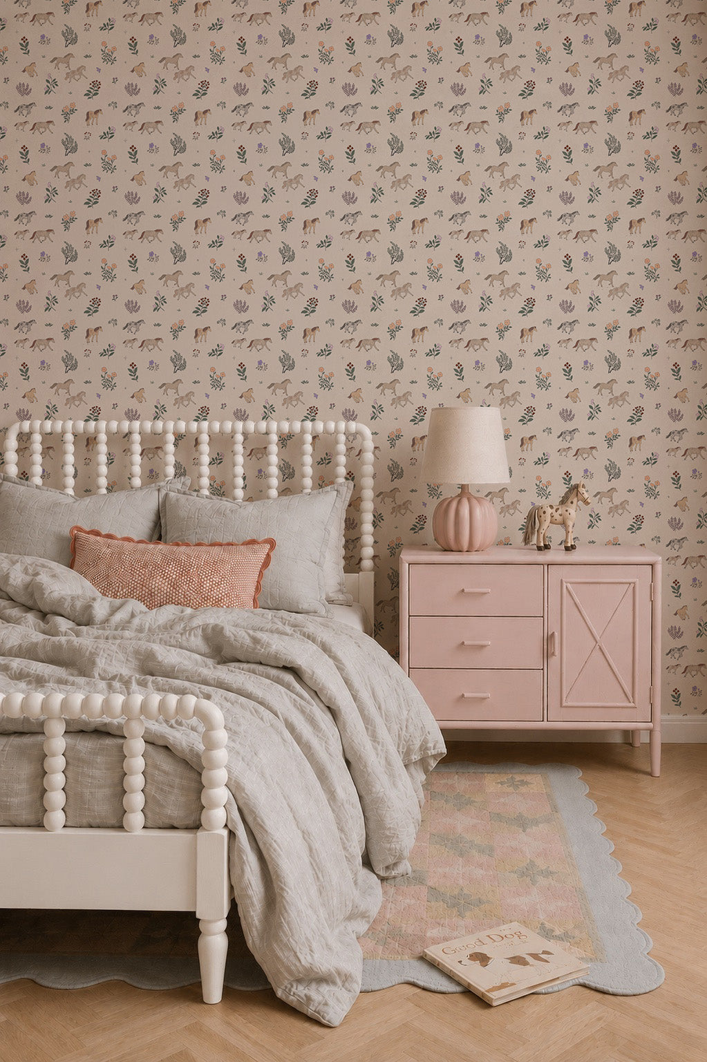 A cozy bedroom features a white spindle bed with gray bedding, a pink pillow, and a pink nightstand topped with a pink lamp and animal figurines. The walls are adorned with Quincy Horses Wallpaper in soft pastel colors for a delicate touch.