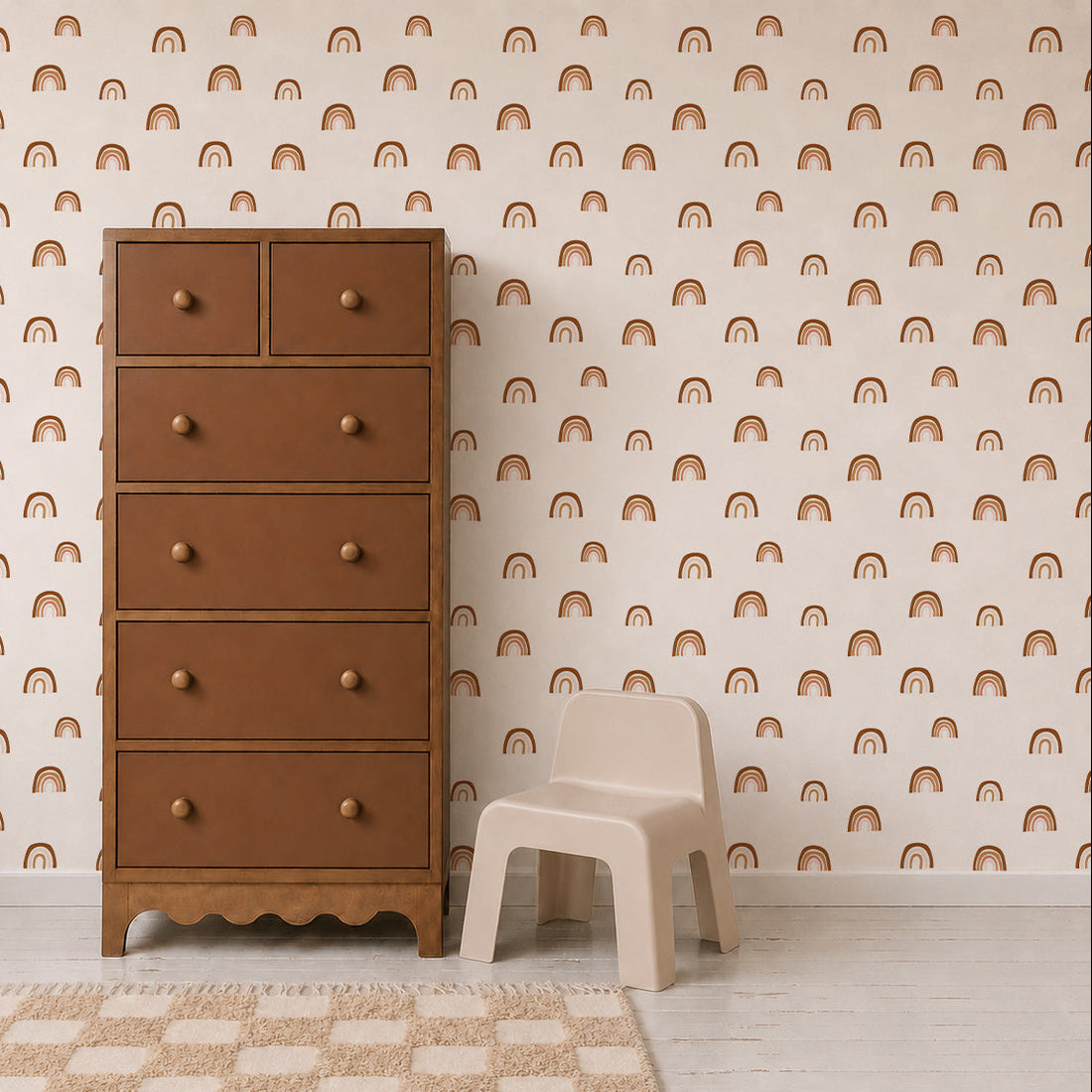 A tall brown dresser stands next to a small beige child’s chair on a light rug. The background wall features repeating pattern wallpaper adorned with simple orange rainbows, identified as the Raining Rainbows Wallpaper.