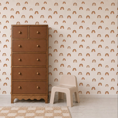 A tall brown dresser stands next to a small beige child’s chair on a light rug. The background wall features repeating pattern wallpaper adorned with simple orange rainbows, identified as the Raining Rainbows Wallpaper.