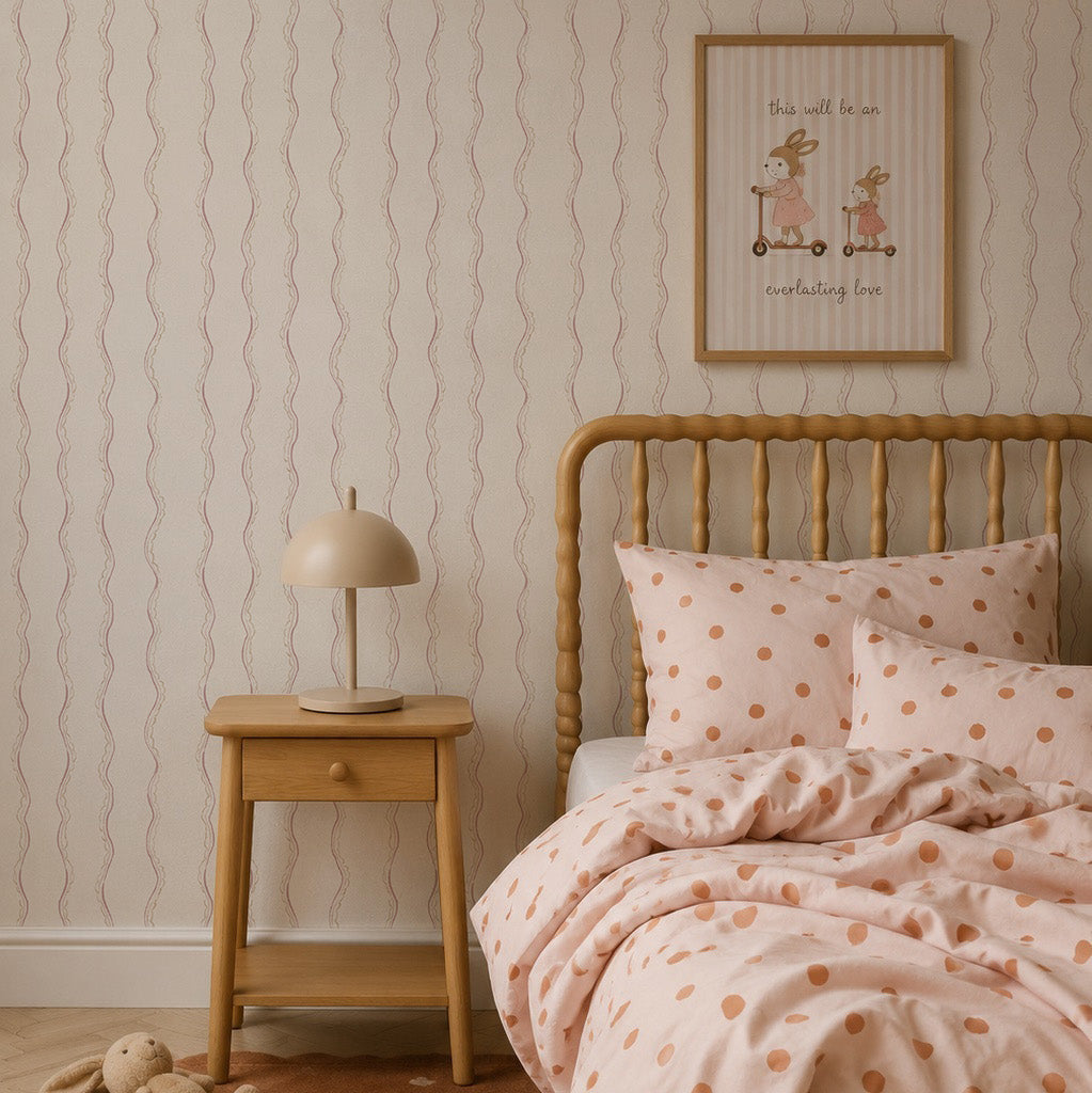 Elegant children’s bedroom featuring a wooden bed with polka dot bedding, a bedside table with a lamp, a stuffed bunny on a brown rug, and framed art displayed on Ribbon Stripe Wallpaper in Rose for a sophisticated touch.