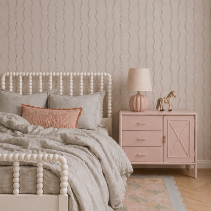A cozy bedroom features a white spindle bed with light gray bedding, a coral pillow, and a pink nightstand topped with a lamp and giraffe figurine. A pastel rug lies on the floor beside a children’s book, while the space is elegantly accented by Ribbon Stripe Wallpaper in Rose adorning the walls.