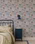 A cozy bedroom features a metal-framed bed, yellow and white striped bedding, a blue nightstand, a wall lamp, and cheerful Rigby Dog Print Wallpaper in blue on a gray background.