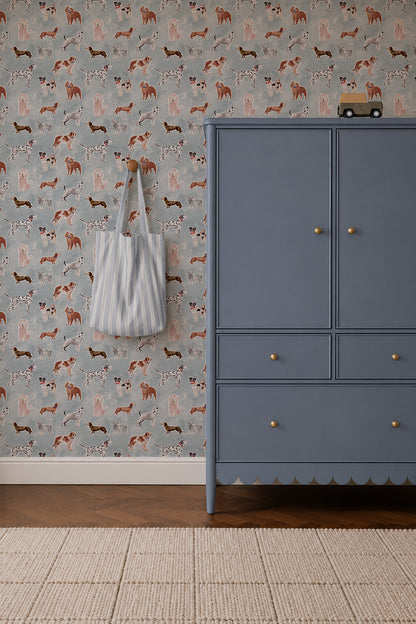 Rigby Dog Print Wallpaper, Blue featuring a repeating pattern of various dog breeds on a blue background, next to a blue armoire and a striped tote bag hanging on the wall.