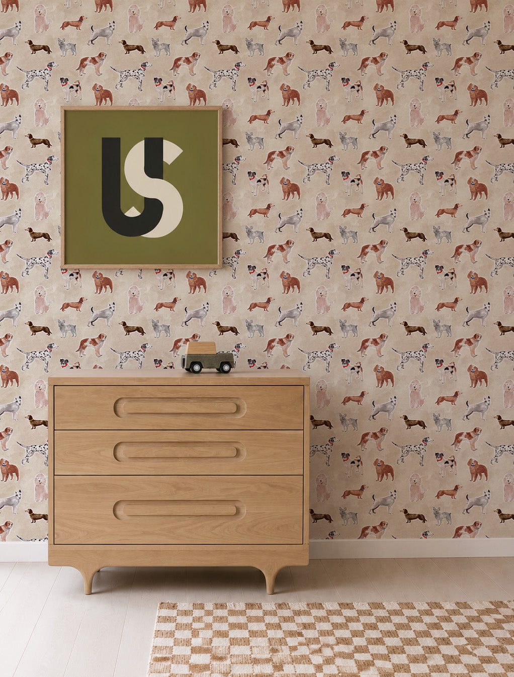 Rigby Dog Print Wallpaper in sand, featuring a repeating pattern of handpainted dog prints, positioned behind a wooden dresser and framed abstract art.