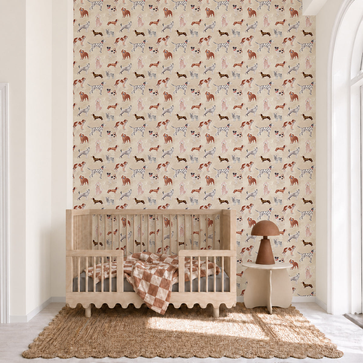 Rigby Dog Print Wallpaper, Sand, featuring a repeating pattern of handpainted dog prints on a sand-colored background, installed behind a wooden crib and side table.