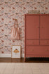 A pink wardrobe stands by a wall covered in Rigby Dog Print Wallpaper, Rose. A striped bag hangs nearby, and a framed muffin illustration rests on the light rug.
