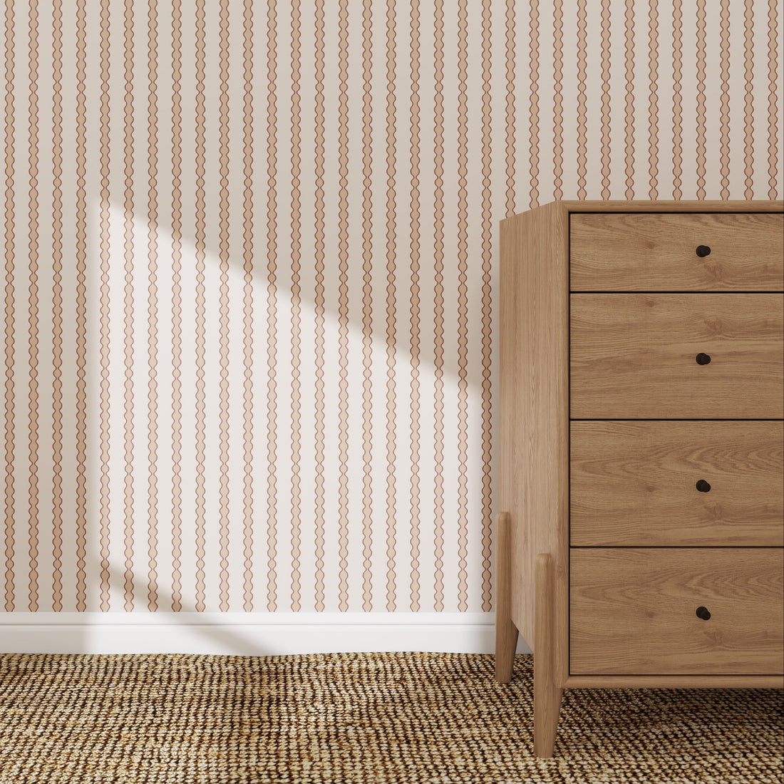 A wooden dresser with five drawers sits on a woven carpet beside a wall adorned with Little Abacus Stripe Wallpaper Sample in Rose. Sunlight casts a triangular shadow, highlighting the elegant pattern and quality of the wallpaper.