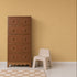 A tall brown wooden dresser stands next to a small, light beige plastic chair, set against the Scallop Shell Mural in yellow with a white polka dot pattern and a light wood floor—perfect for brightening up any kids playroom.