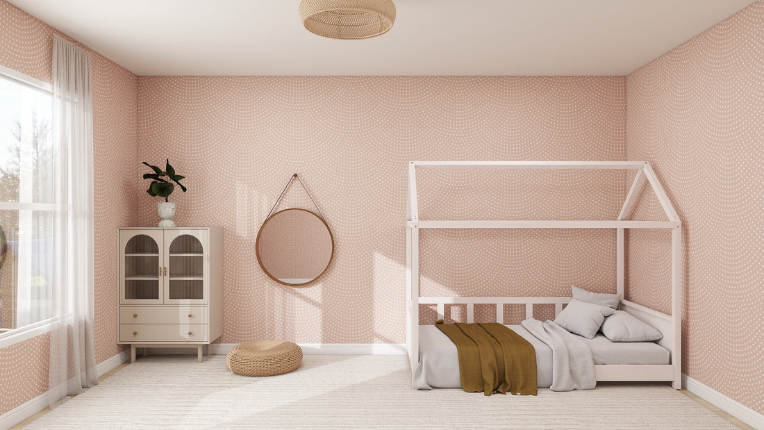A cozy, minimalist childrens bedroom features Scallop Wallpaper Repeat Pattern | Rose, a white house-frame bed with pillows and blanket, a round mirror, cabinet with plants, woven pouf, and large windows filling the space with natural light.