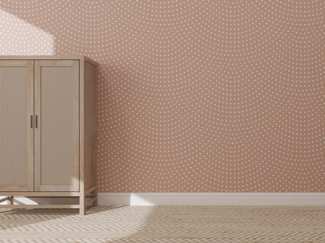 A wooden cabinet stands against a pink wall adorned with Scallop Shell Wallpaper Repeat Pattern | Rose. Sunlight from the left highlights the cabinet and the light herringbone floor, enhancing the tonal pink hues of the space.