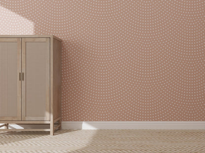 A wooden cabinet stands against a pink wall adorned with Scallop Shell Wallpaper Repeat Pattern | Rose. Sunlight from the left highlights the cabinet and the light herringbone floor, enhancing the tonal pink hues of the space.