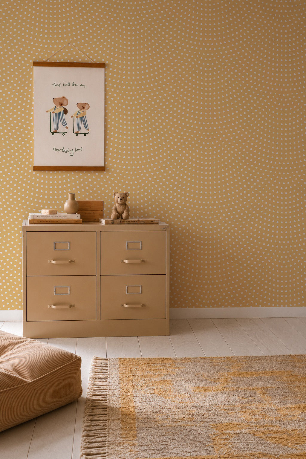 A cozy, minimalist room features the Scallop Shell Mural in yellow as a playful accent wall, a beige four-drawer cabinet, teddy bear, decor items, framed art, patterned rug, and soft pouf on light wooden floors.