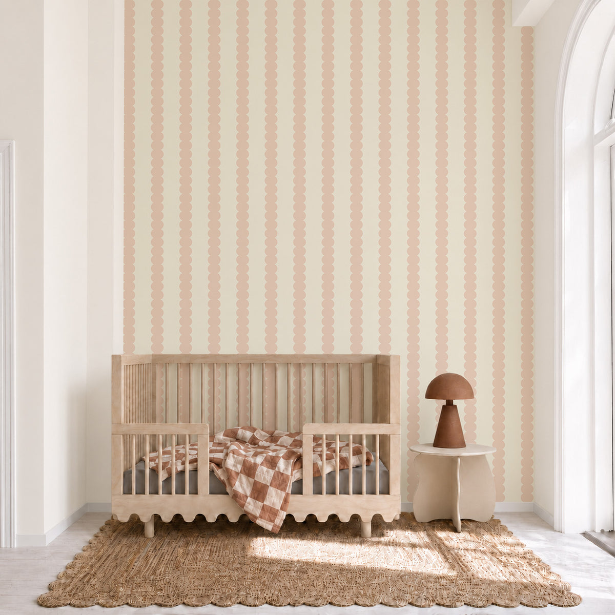 Blush Scallop Stripe Wallpaper featuring vertical scalloped stripes applied to a wall behind a wooden crib and side table.