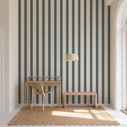 A wooden desk, chair, and pink bench set against Scallop Stripe Wallpaper, Deep Blue, featuring vertical rows of scalloped circles on a light cream background.