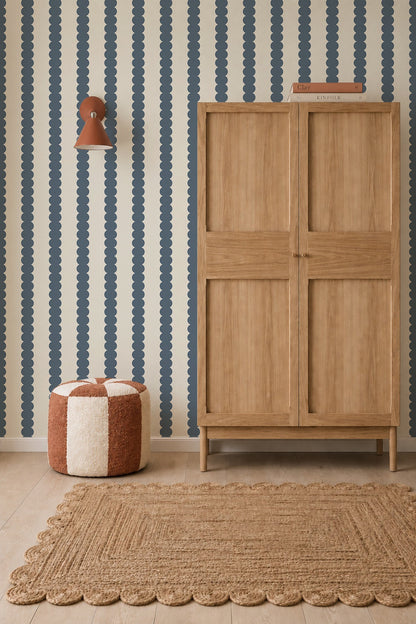 A room featuring Scallop Stripe Wallpaper, Deep Blue in deep blue against an off-white background, complete with a wooden cabinet, a checkered ottoman, and a textured area rug.