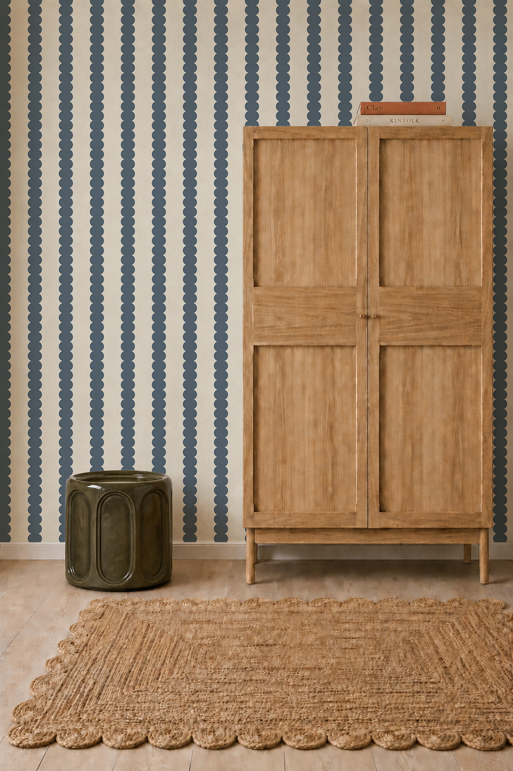 Scallop Stripe Wallpaper, Deep Blue, featuring a vertical pattern of blue scallops against a light background, displayed behind a wooden wardrobe and a dark ceramic stool.