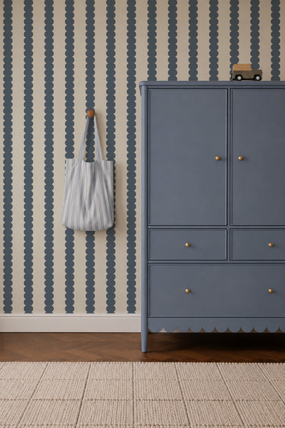 Scallop Stripe Wallpaper, Deep Blue features vertical scalloped patterns on a cream background, positioned next to a blue cabinet with a striped tote bag hanging on the wall.