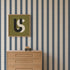 Scallop Stripe Wallpaper, Deep Blue featuring vertical stripes of overlapping circles on a light background, displayed behind a wooden dresser with a small toy car and a framed abstract letter S.