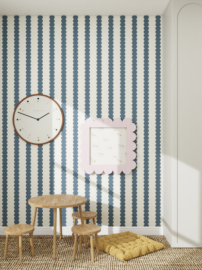 A children’s playroom with a small wooden table and stools, a yellow floor cushion, a large wall clock, a framed picture, and Scallop Stripe Wallpaper Deep Blue—ideal for creating a cozy nursery atmosphere.