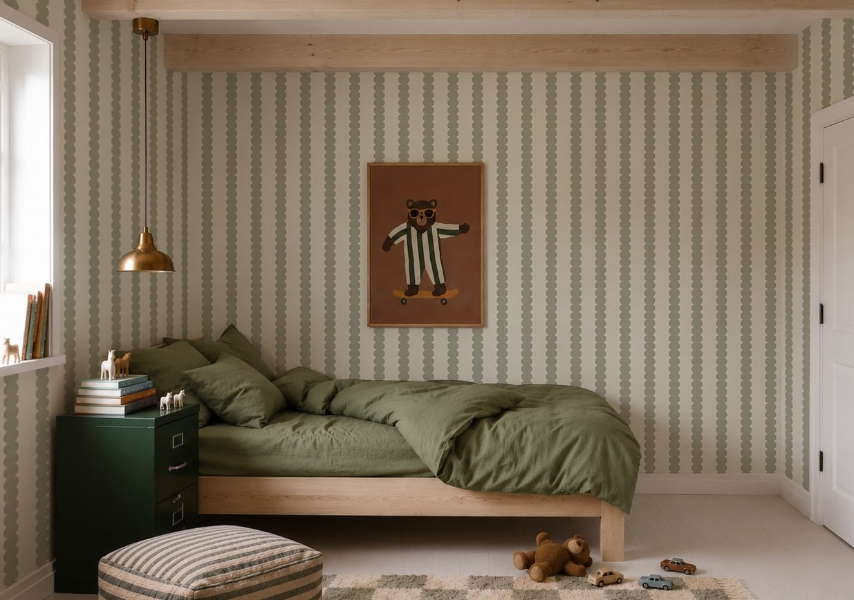 A cozy bedroom featuring a green bed, Scallop Stripe Wallpaper in Green, a bear illustration on the wall, a gold lamp, green cabinet, books, a striped ottoman, and toys on the floor. Soft natural light comes from a window on the left.