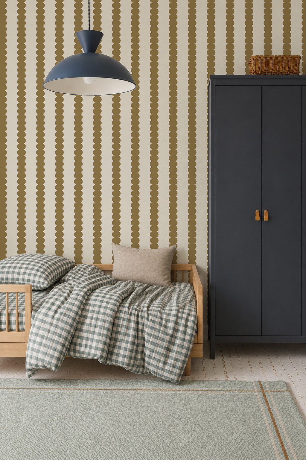 A cozy children’s room features a small wooden bed, checkered bedding, a beige pillow, a tall dark blue wardrobe, and Scallop Stripe Wallpaper in Moss. A large blue pendant lamp hangs overhead.