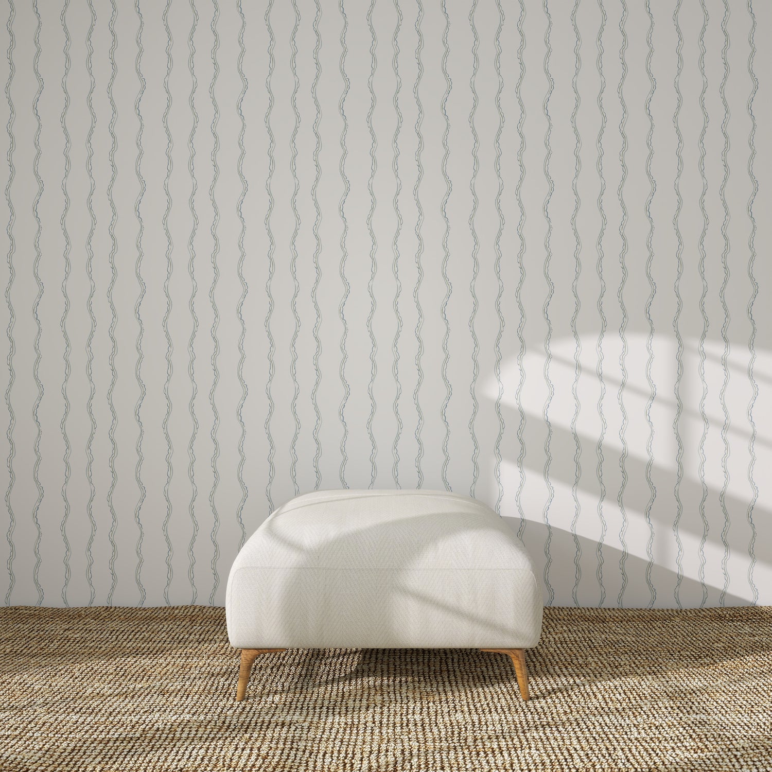 A white upholstered bench sits on a woven rug in front of a light wall covered with Ribbon Stripe Wallpaper, Blue. Sunlight from the right casts geometric shadows across the wall.