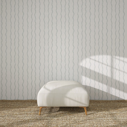 A white upholstered bench sits on a woven rug in front of a light wall covered with Ribbon Stripe Wallpaper, Blue. Sunlight from the right casts geometric shadows across the wall.