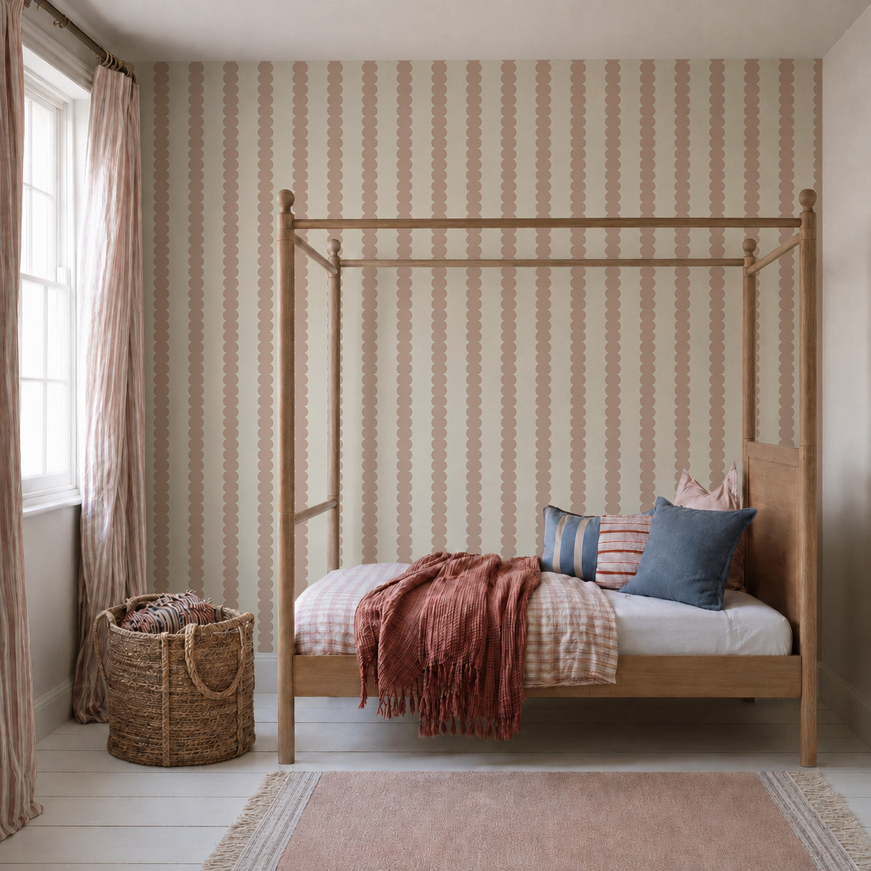 A cozy bedroom featuring a wooden canopy bed, Scallop Stripe Wallpaper in Pink, throw pillows, a pink blanket, a woven basket, sheer curtains, and a soft pink rug on white wooden floors. Sunlight streams in through the window.