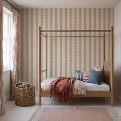 A cozy bedroom featuring a wooden canopy bed, Scallop Stripe Wallpaper in Pink, throw pillows, a pink blanket, a woven basket, sheer curtains, and a soft pink rug on white wooden floors. Sunlight streams in through the window.