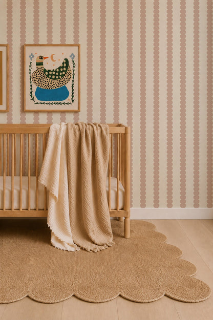 A wooden crib with beige blankets draped over the side sits on a scalloped rug. The wall behind features Scallop Stripe Wallpaper, Pink, and two framed animal art prints.