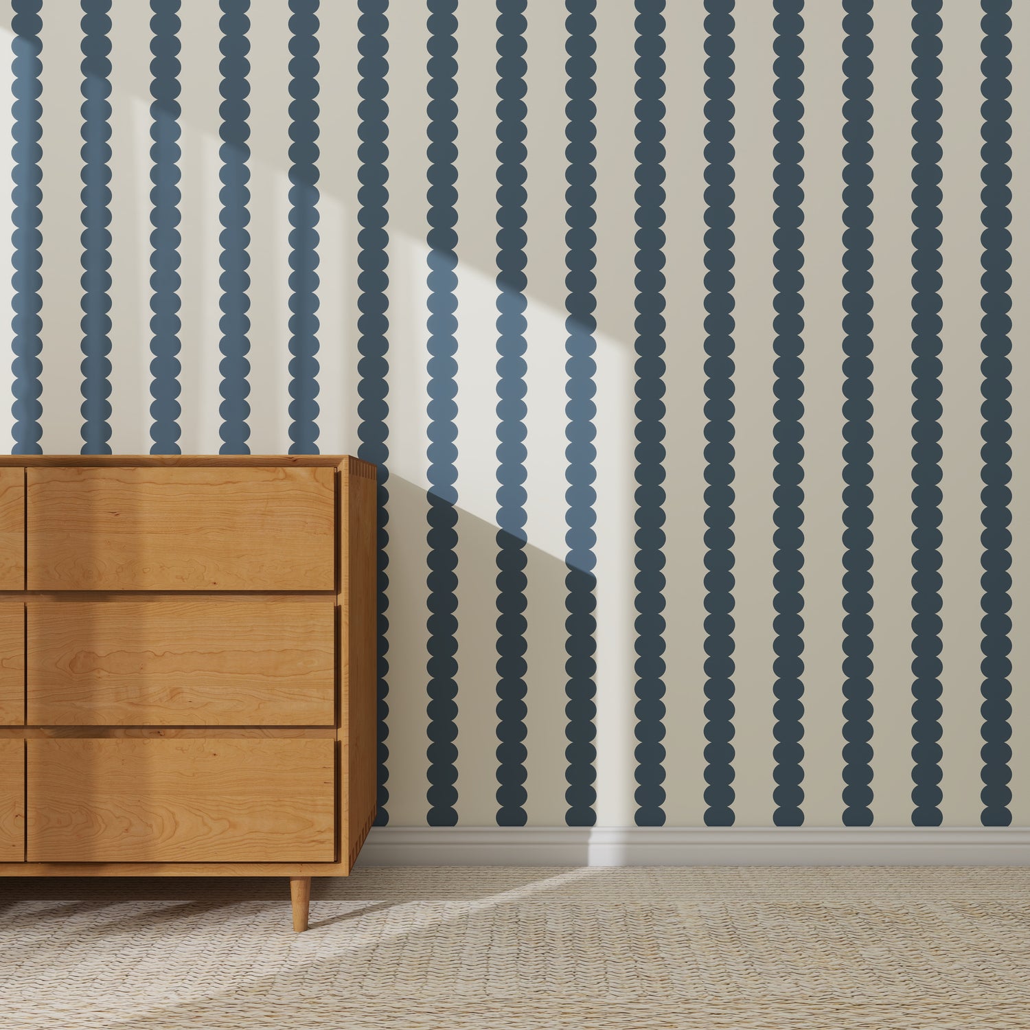 A wooden dresser sits on a woven rug before a wall covered with Scallop Stripe Wallpaper Deep Blue, sunlight casting diagonal shadows across the surface.
