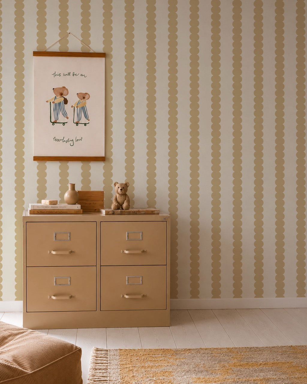 A beige dresser with four drawers stands against a wall adorned with Scallop Stripe Wallpaper in Yellow. A teddy bear and decor sit on top, while a framed artwork featuring two animals and handwritten text hangs above. A rug is visible in the foreground.