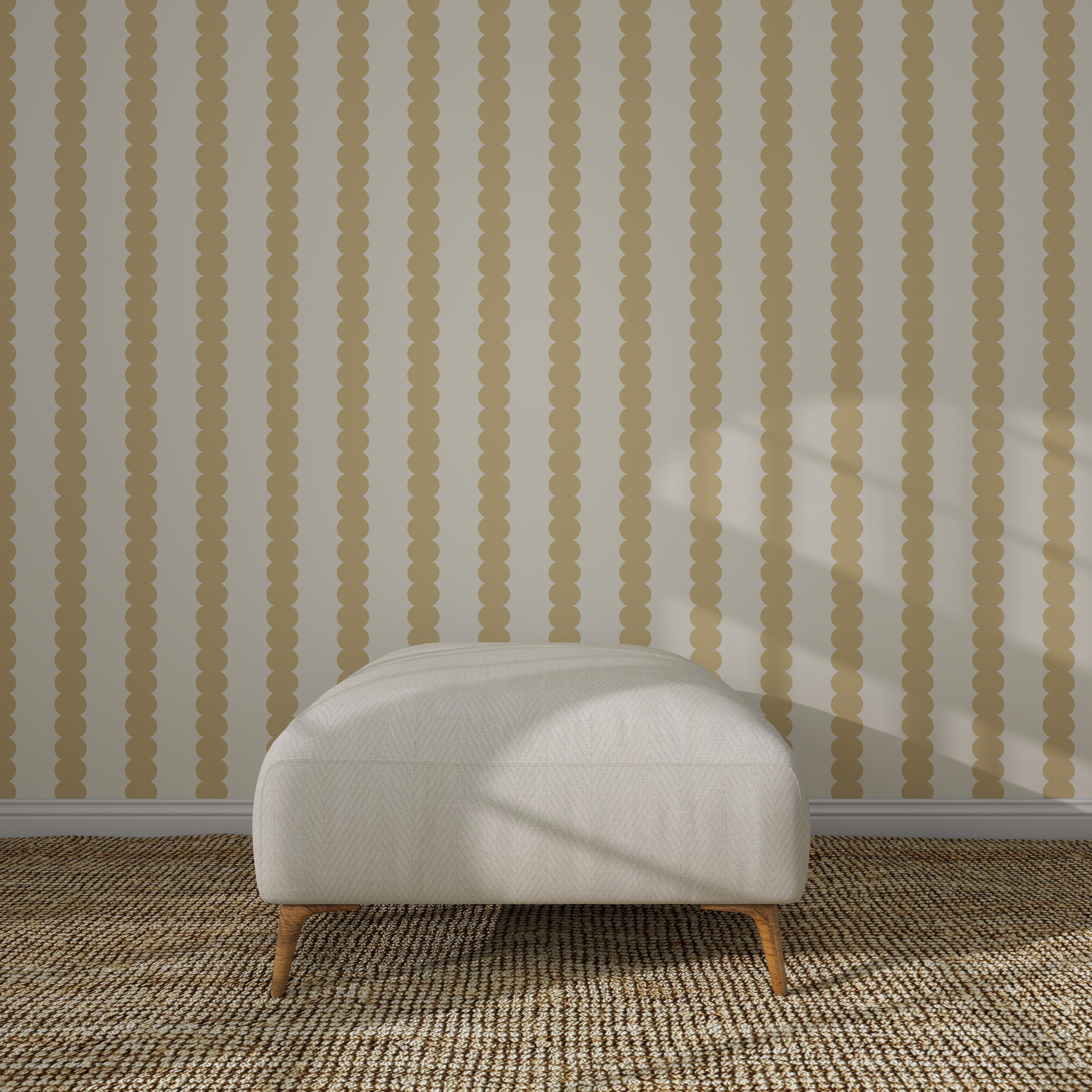 A white cushioned ottoman with wooden legs sits on a woven rug before a beige wall decorated with Scallop Stripe Wallpaper Sample, Yellow, its vertical scalloped stripes highlighted by sunlight casting shadows on the scene.