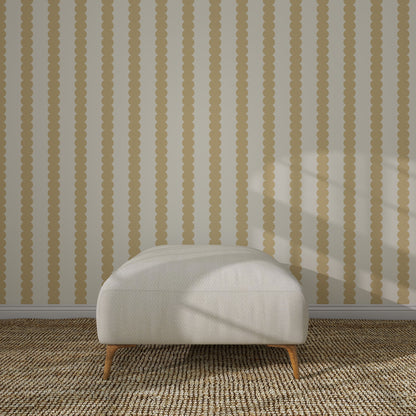 A white cushioned ottoman with wooden legs sits on a woven rug before a beige wall decorated with Scallop Stripe Wallpaper Sample, Yellow, its vertical scalloped stripes highlighted by sunlight casting shadows on the scene.