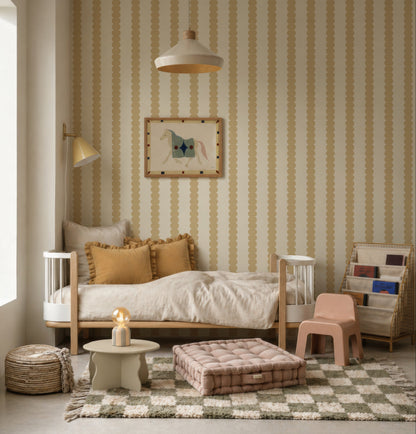 A cozy kids’ room featuring Scallop Stripe Wallpaper, Yellow, a small bed with mustard pillows, wall lamp, framed art, striped rug, basket, beige side table with lamp, tufted floor cushion, and a book rack filled with books.