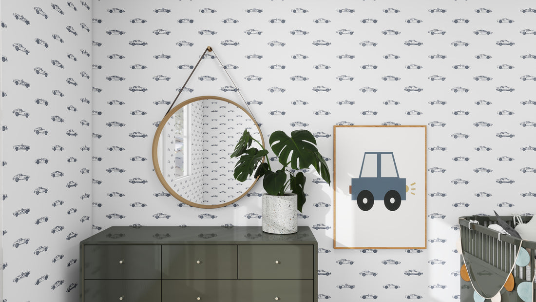 A nursery features munks and mes Vintage Cars Wallpaper Repeat Pattern, a round mirror, and a potted plant on a dark green dresser. A framed car illustration hangs beside the mirror, with a crib partially visible on the right.