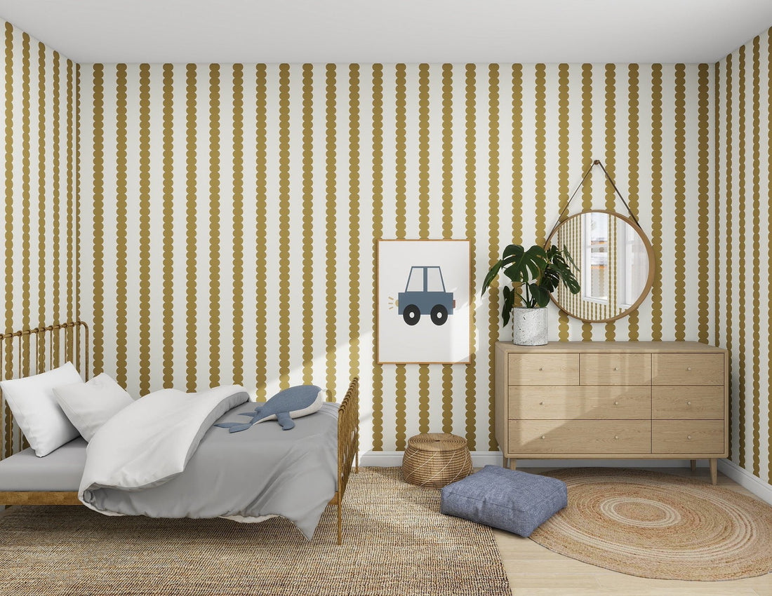 A cozy bedroom featuring Scallop Stripe Wallpaper Moss by munks and me in gold and white stripes. A wooden bed with gray bedding, a stuffed whale toy, a framed car picture, and a round mirror above the dresser with a plant. A wicker basket and round rug complete the kids room decor.