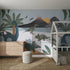 Children’s bedroom featuring the Dinosaur and Friends Wallpaper Mural with colorful dinosaurs, volcanoes, and palm trees. Includes a wooden dresser, white bunk bed, round ottoman, and woven rug for a playful nursery space.
