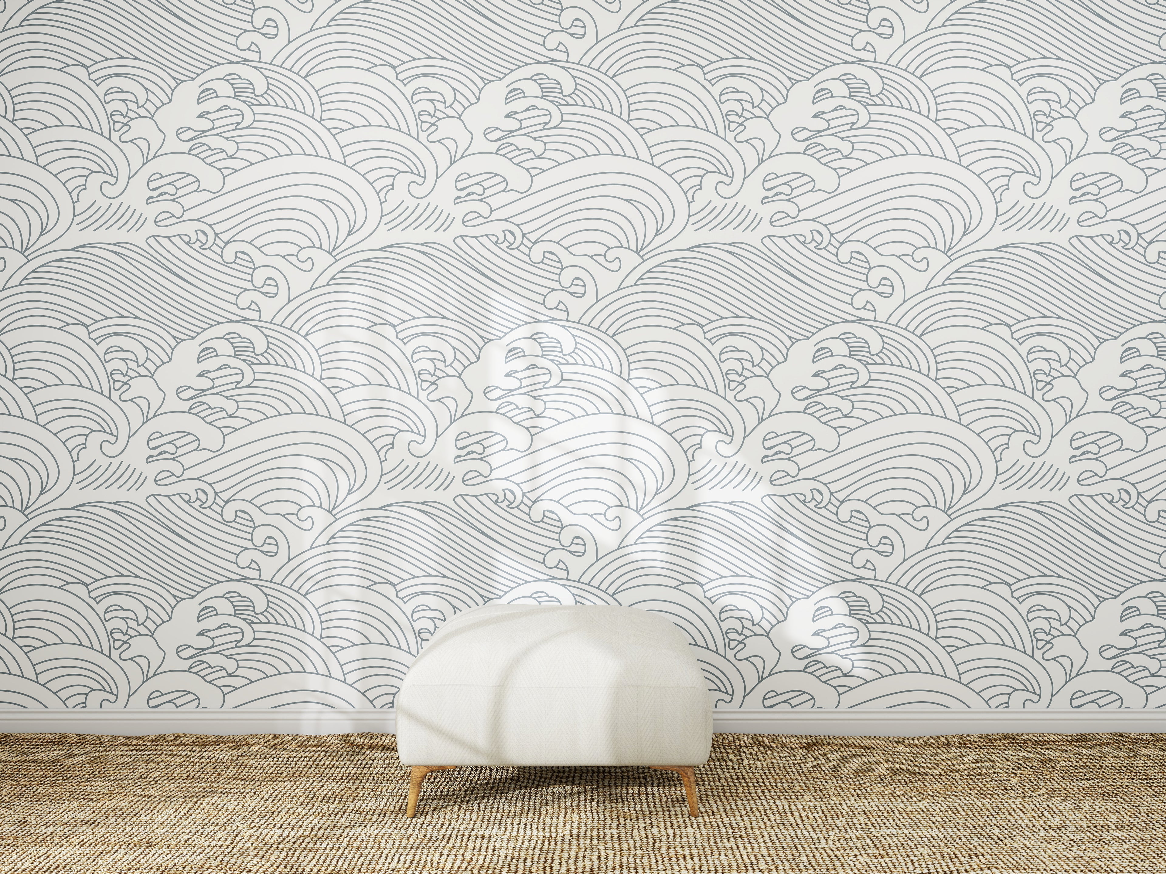 A white ottoman sits on a woven rug in front of a wall decorated with Making Waves Wallpaper, which displays a repeating pattern of hand-drawn gray ocean waves on a white background.