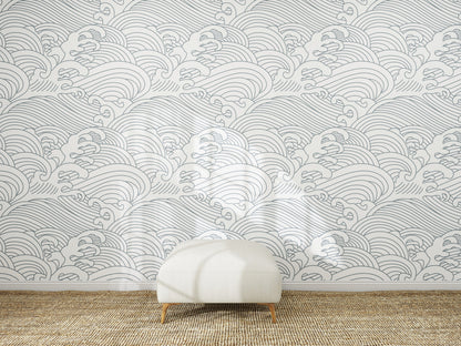 A white ottoman sits on a woven rug in front of a wall decorated with Making Waves Wallpaper, which displays a repeating pattern of hand-drawn gray ocean waves on a white background.