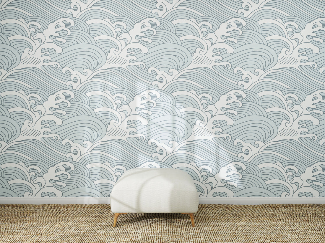 A white ottoman sits on a woven rug in front of a wall covered with Making Waves Wallpaper | Blue. Sunlight creates soft shadows on the floor and wallpaper mural.