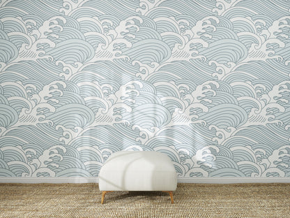 A white ottoman sits on a woven rug in front of a wall covered with Making Waves Wallpaper | Blue. Sunlight creates soft shadows on the floor and wallpaper mural.